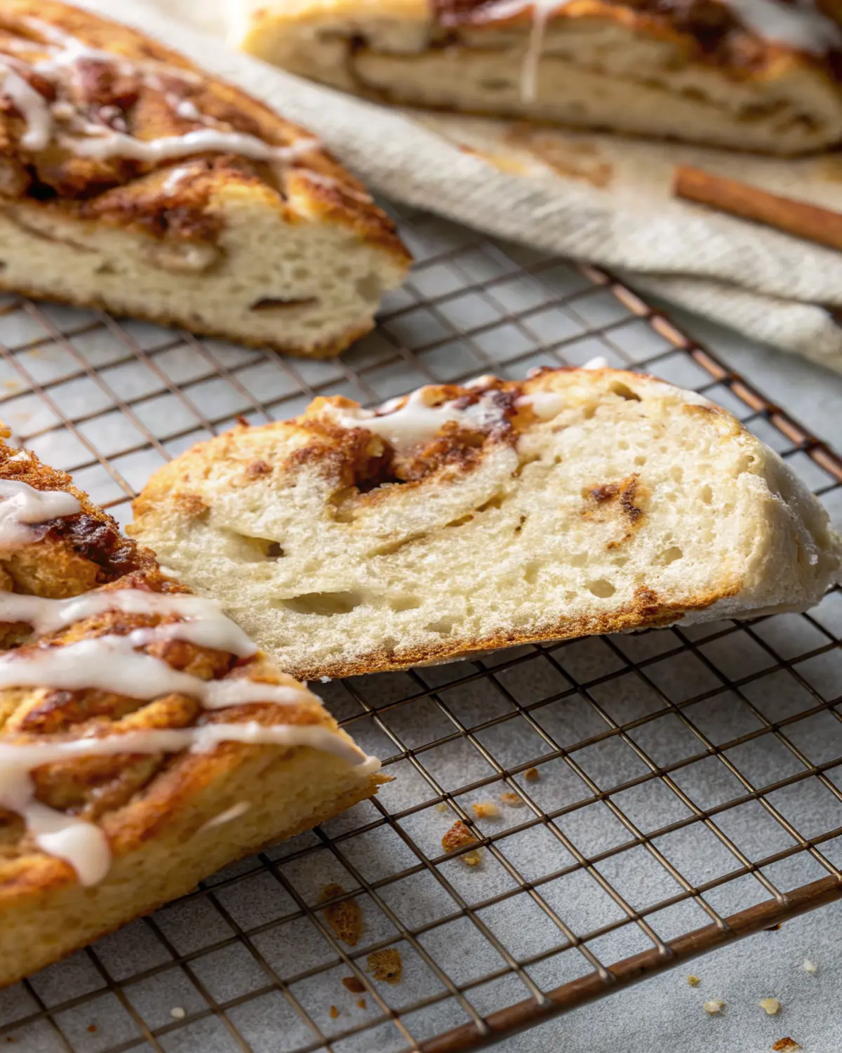 cinnamon roll focaccia slice with cinnamon Close-up of a cinnamon roll focaccia slice with cinnamon swirls and icing drizzle on a wire rack.