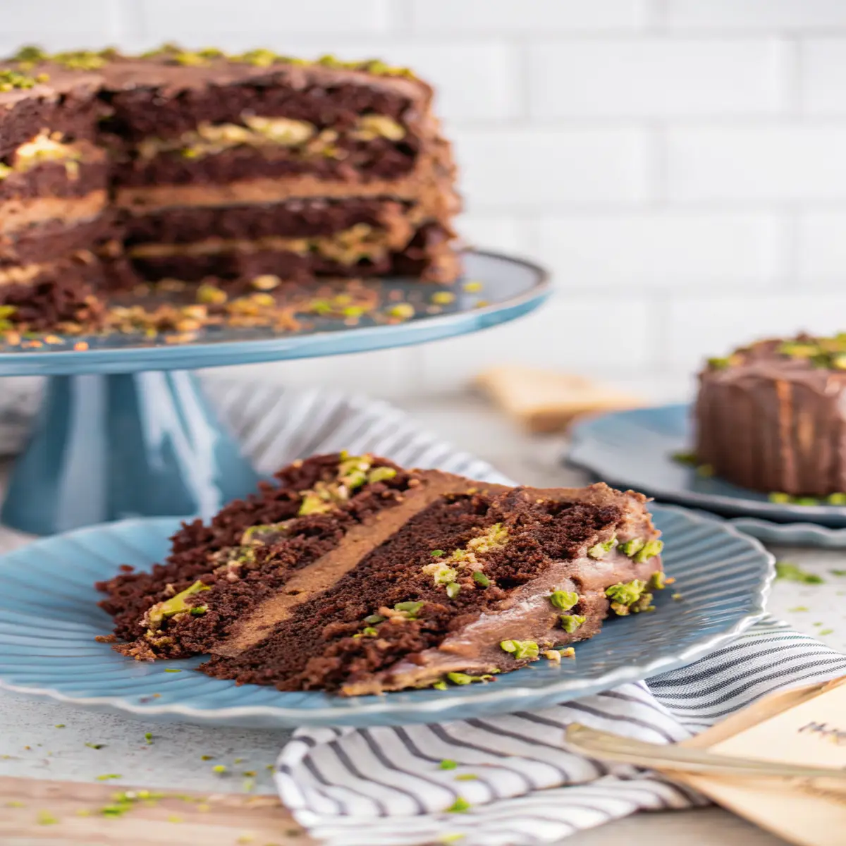 A slice of Dubai chocolate cake with pistachio filling and chocolate frosting on a ceramic plate
