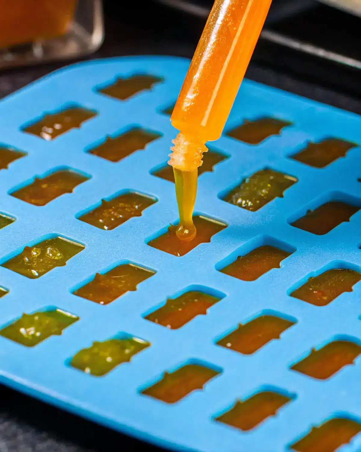 healthy-jelly-sweets-dropper-mold Close-up of orange liquid being dropped into a gummy bear mold to make healthy jelly sweets