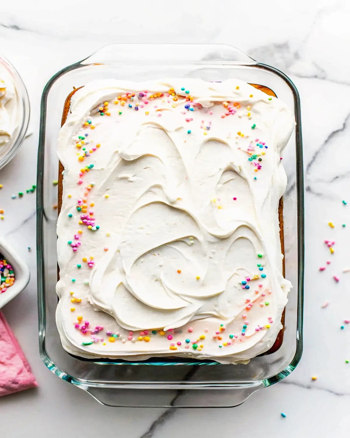 vanilla-quarter-sheet-cake-rainbow-sprinkles Frosted vanilla quarter sheet cake with rainbow sprinkles in a glass baking dish
